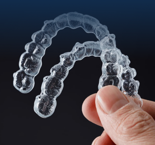 Clear plastic dental aligners held in hand against dark background for orthodontic treatment.