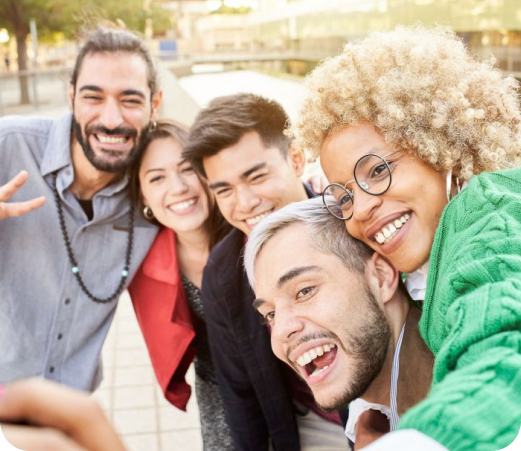 Diverse group of smiling people taking a selfie together outdoors in sunny setting.