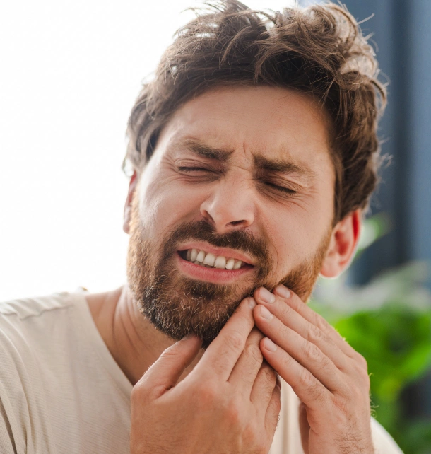 Man experiencing tooth pain, holding cheek outdoors in dental care context.