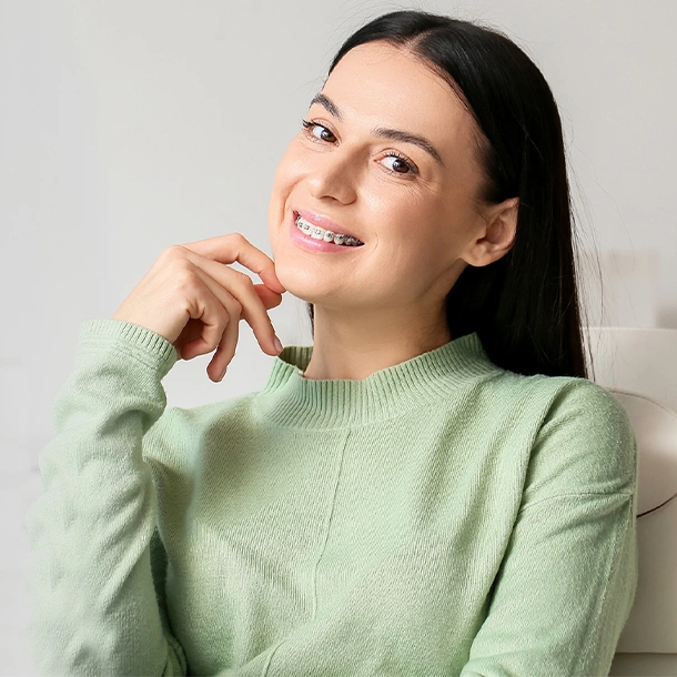 Woman in light green sweater smiling with hand near face against white background.