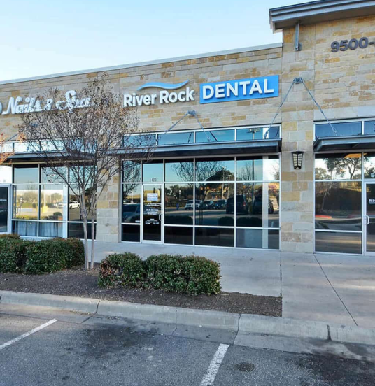 River Rock Dental storefront with blue signage, glass entrance doors, and landscaping in Austin.