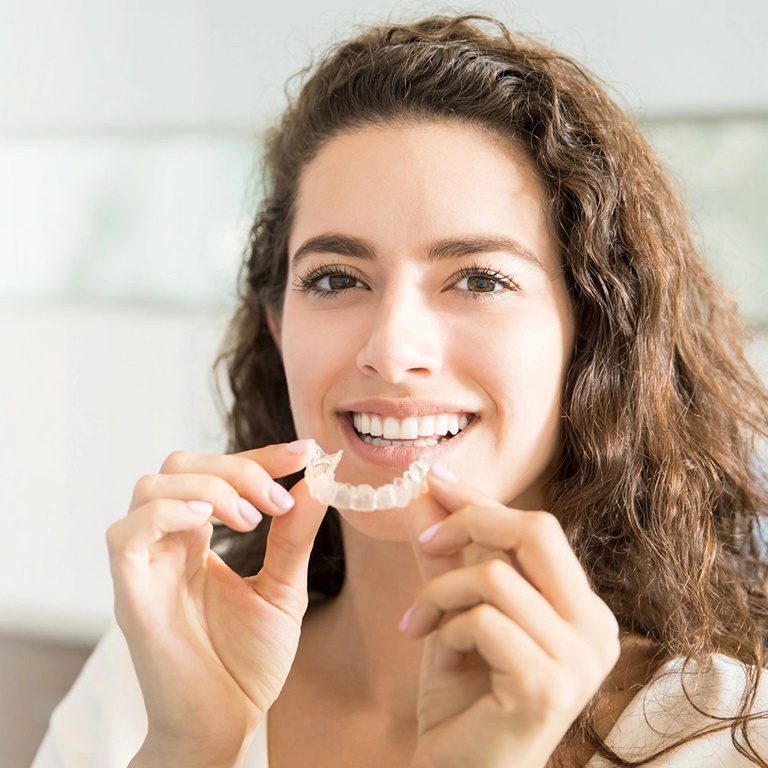 Woman holding clear dental aligners, smiling in bright indoor setting.