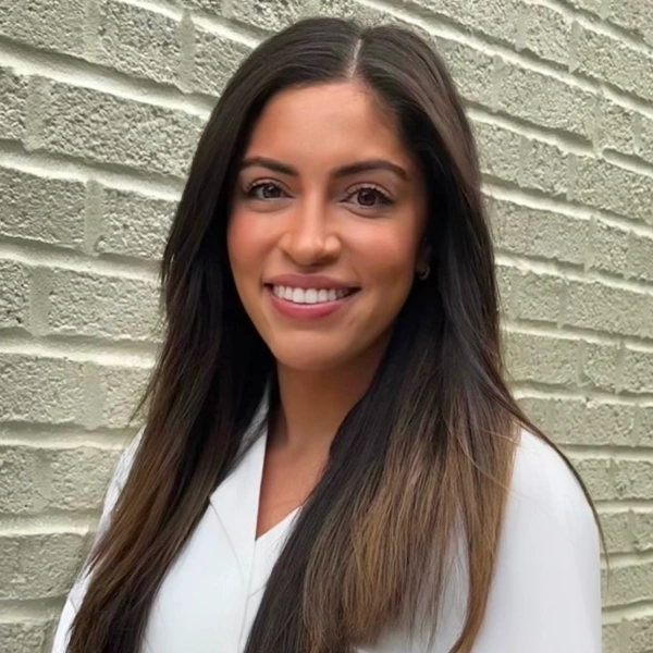 Professional woman smiling at camera against brick wall, dental practice staff portrait.